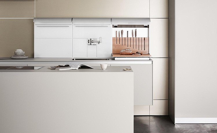 Floor-standing, white kitchen island as a connecting element between the living space and multi-functional wall